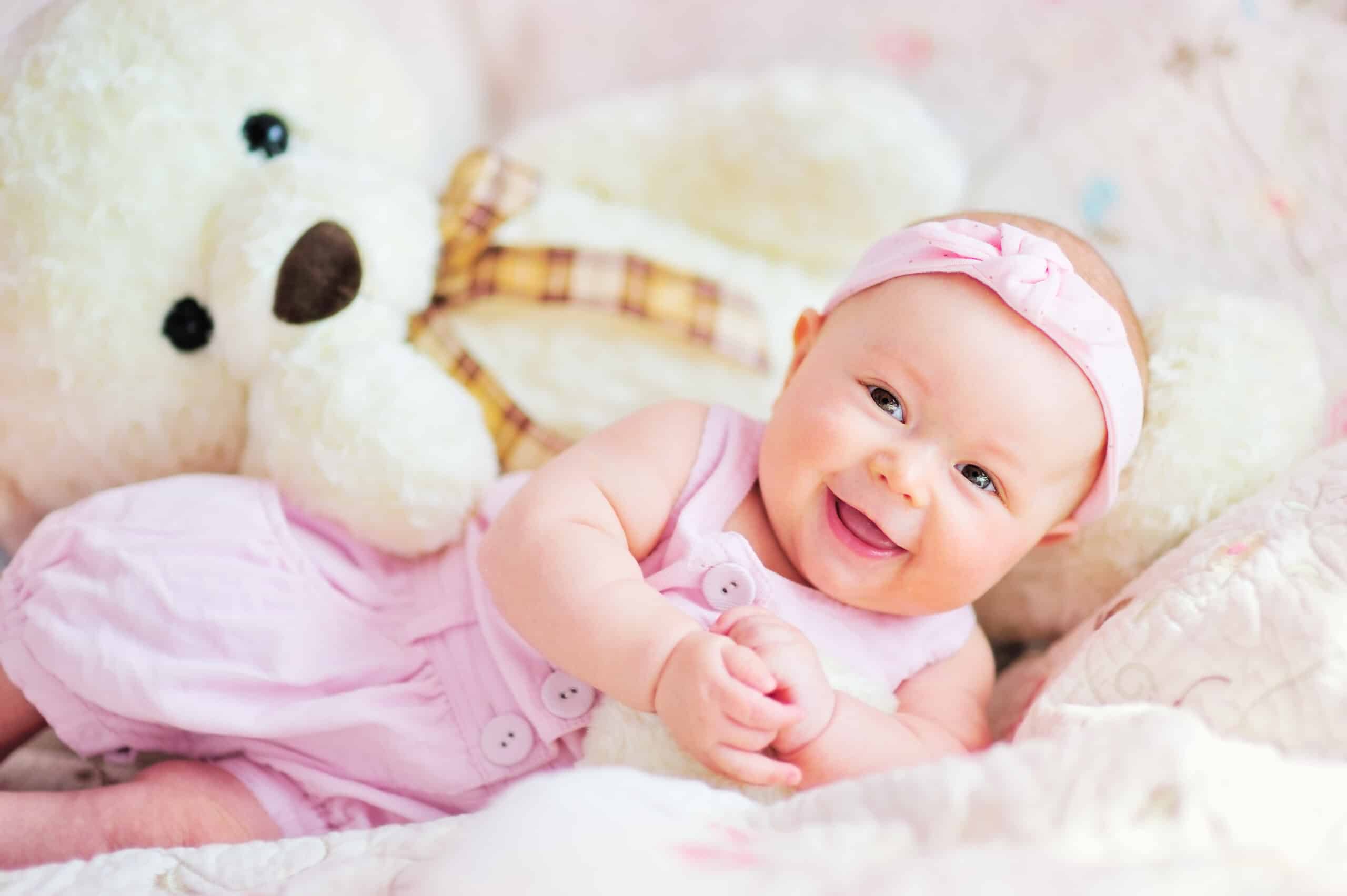 pretty smiling baby girl and teddy bear lying in the bed