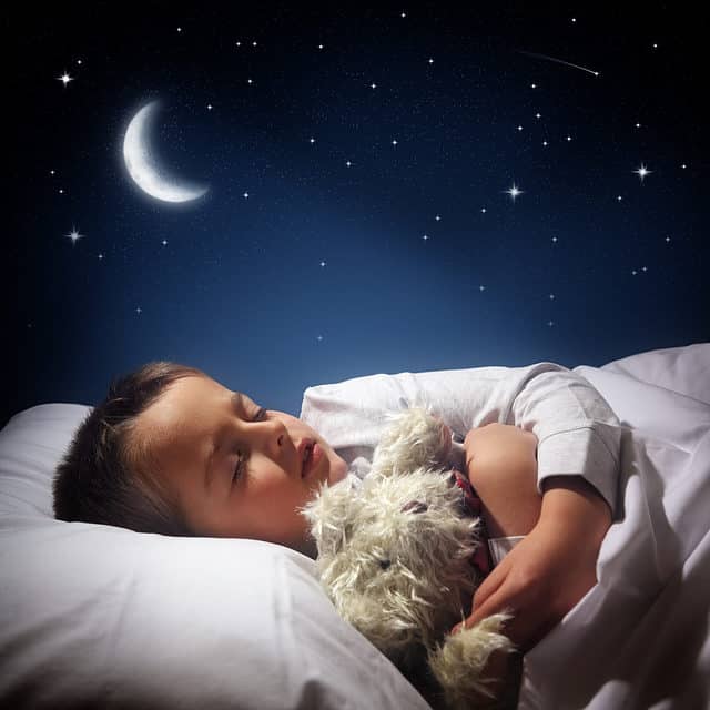 Child sleeping and dreaming in his bed under the moon, stars and blue night sky