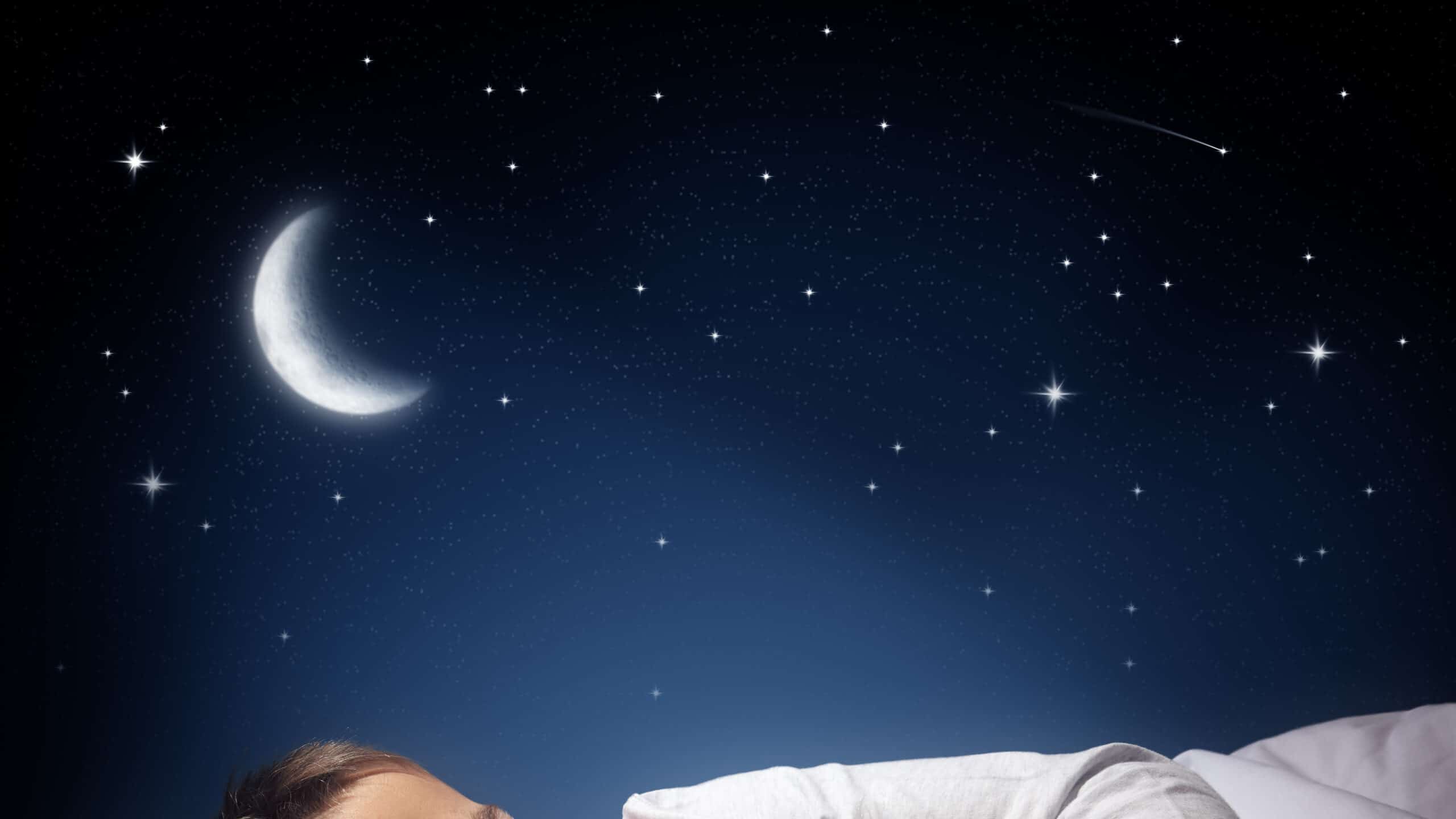 Child sleeping and dreaming in his bed under the moon, stars and blue night sky