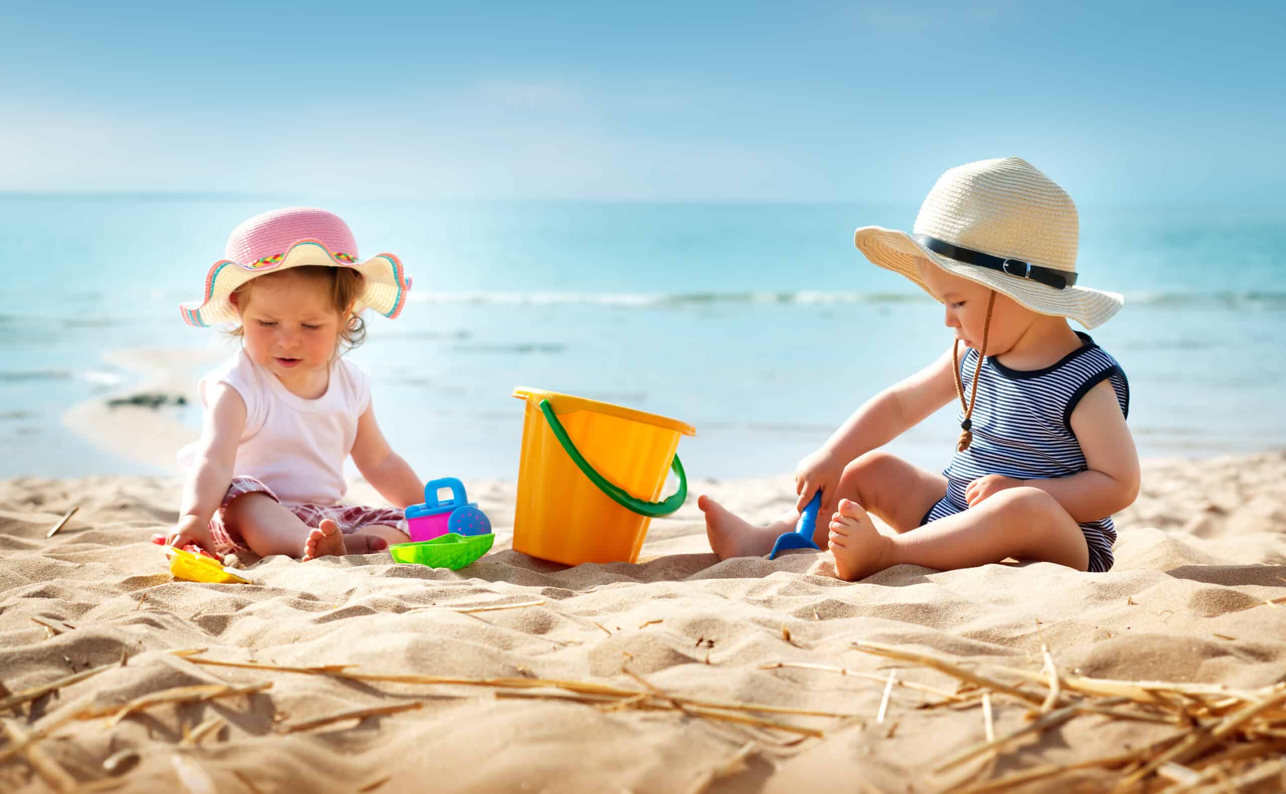 Babygirl and babyboy sitting on the beach in straw hats