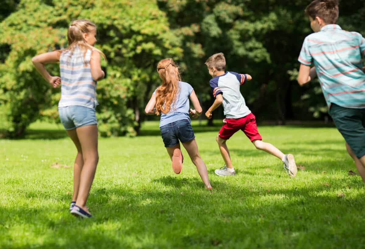 friendship, childhood, leisure and people concept - group of happy kids or friends playing catch-up game and running in summer park