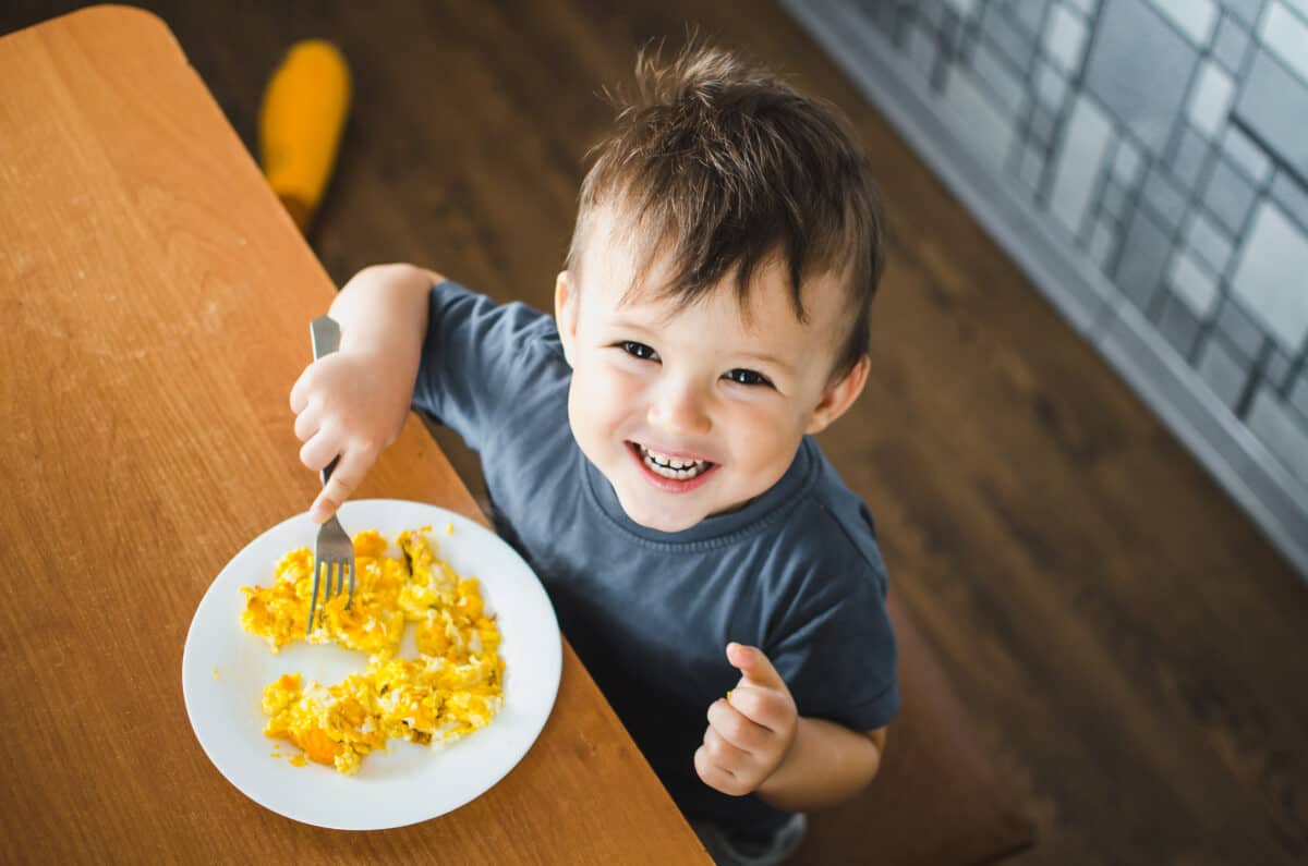 a child in a t-shirt in the kitchen eating an omelet, a fork