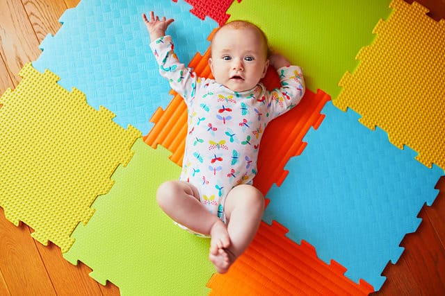 4 months old baby girl lying on colorful play mat on the floor. Activity carpet for kids