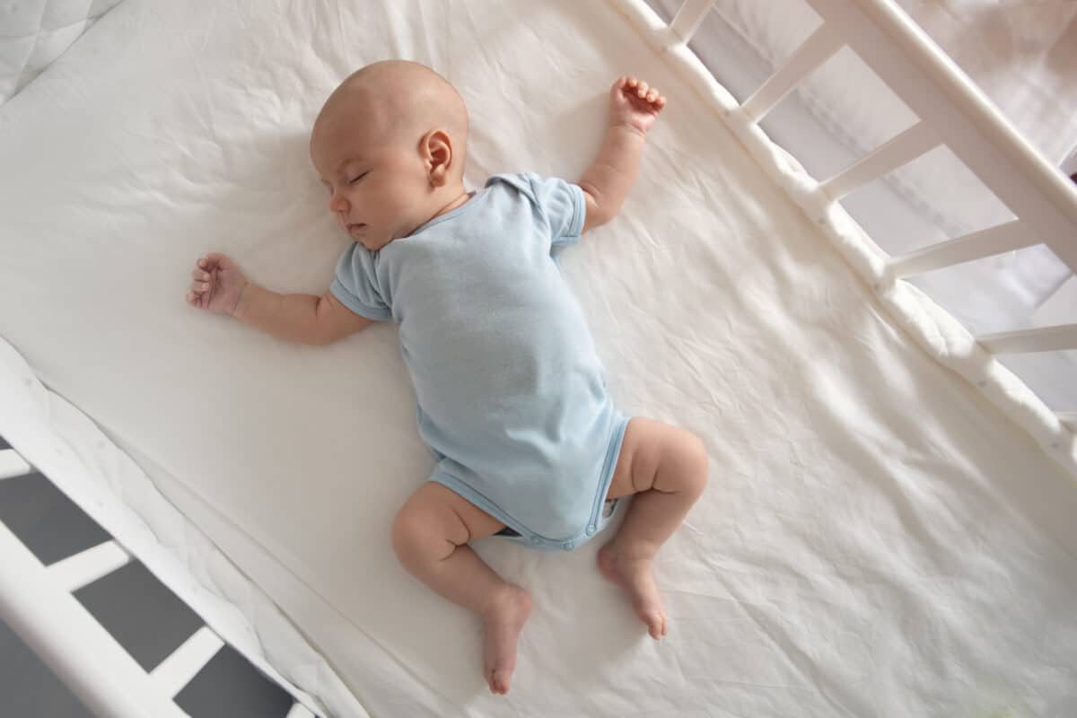 Top view wide angle sleeping newborn baby lies in a crib arms and legs outstretched, baby sleep