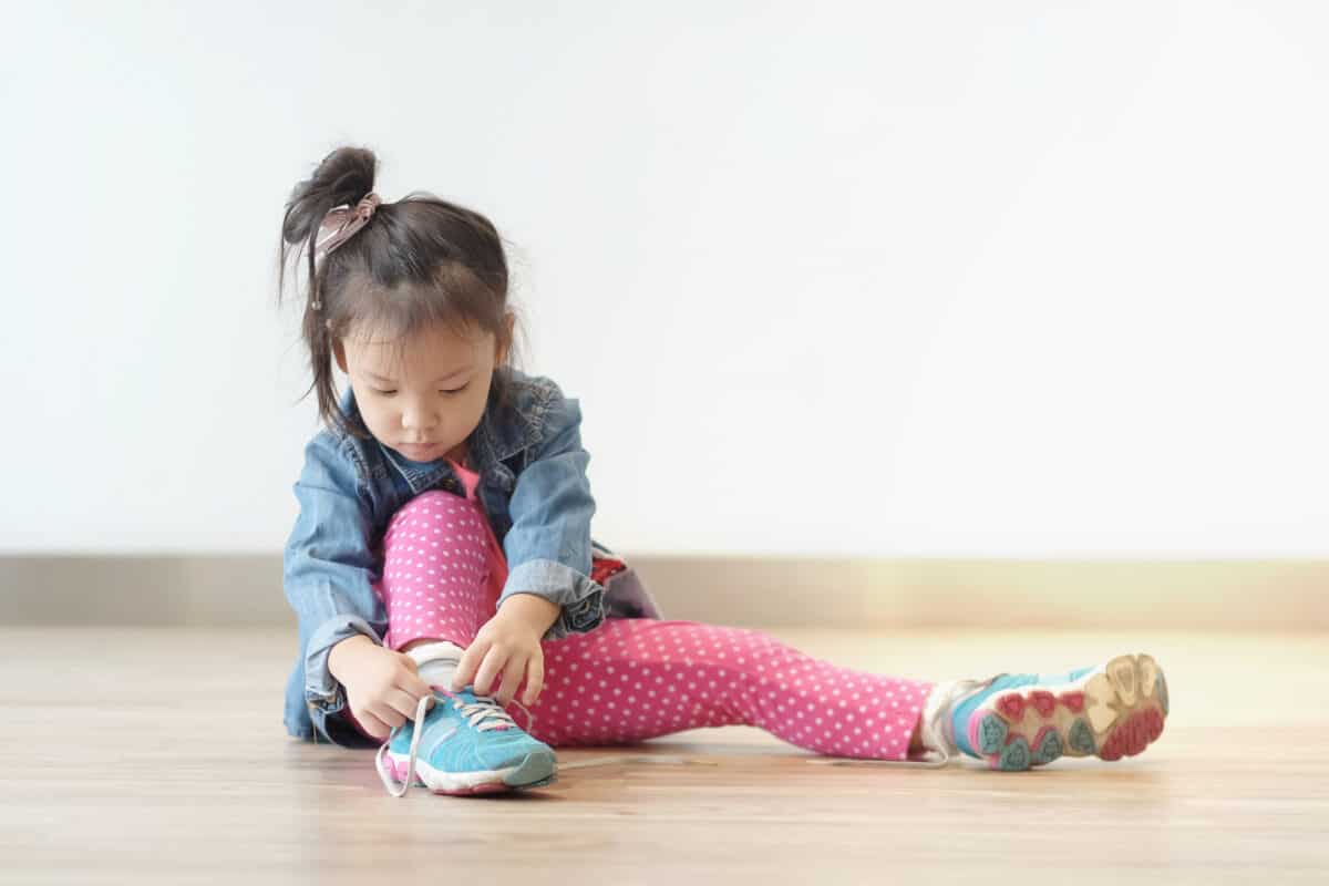 Copy space and Soft focus portrait cute little Asian girl 3 year old sit on the ground and try to tie her shoes. Beautiful kid try to shoelace by herself. concept first step , growth up and moving on.