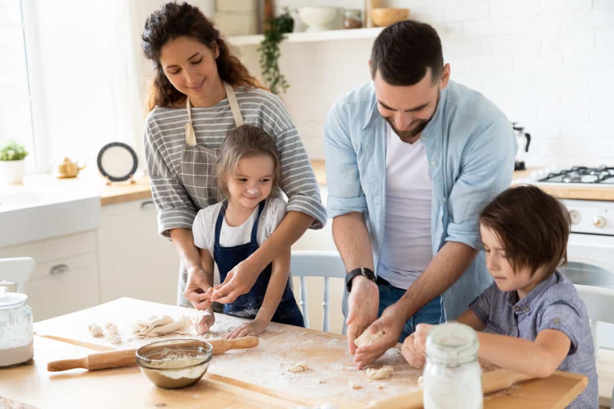 Happy young family with cute little preschooler kids have fun making dough baking pie or pastry in modern kitchen together, overjoyed parents teach small children doing bakery cooking at home