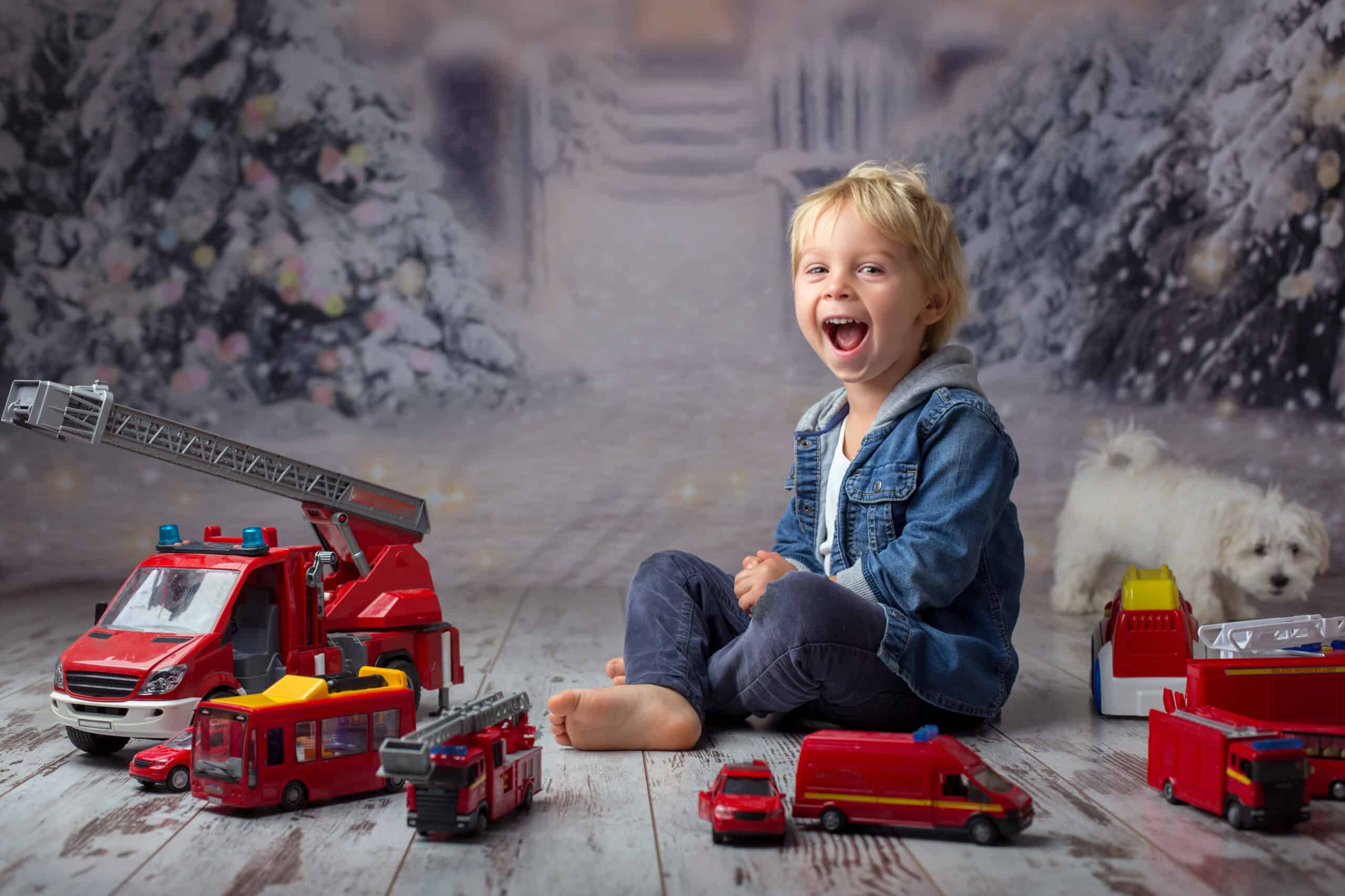 Child, toddler blond boy, playing with fire trucks on the floor at home