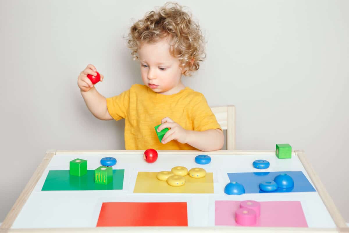Toddler playing with learning toys at home or kindergarten. Baby sorting organising objects blocks with specific colors. Early age education. Kids hand brain development activity for preschoolers.