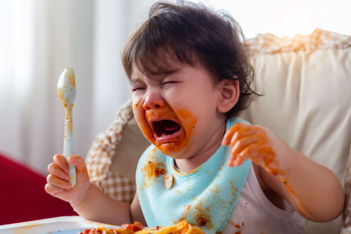 Wayward little toddler child or infant baby crying that don't want eating food on baby chair Cute infant children get hungry and want new food Children get dirty Kid get tantrum Baby is stubborn baby