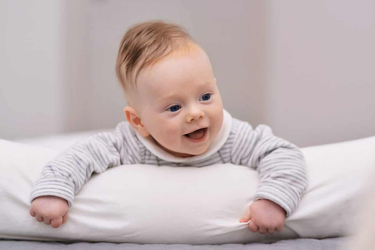 Adorable baby boy in white sunny bedroom. Newborn child relaxing on a bed. Nursery for young children. Furniture, textile and bedding for kids. New born kid during tummy time with toys.