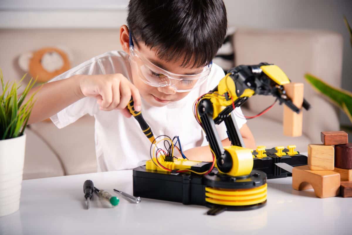 Child learning repairing getting lesson control robot arm, Happy Asian little kid boy using screwdriver to fixes screws robotic machine arm in home workshop, Technology future science education