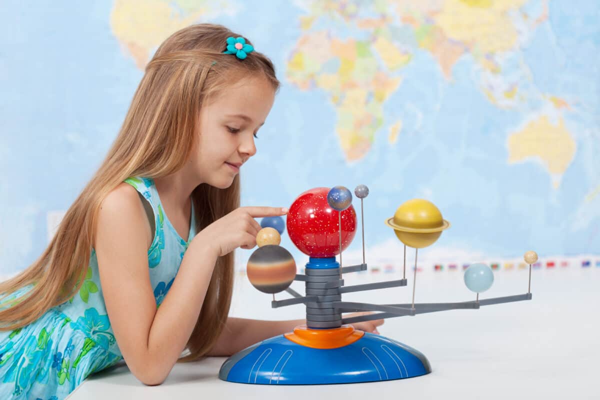 Little girl studies the solar system in geography class - looking at the scale model of planets