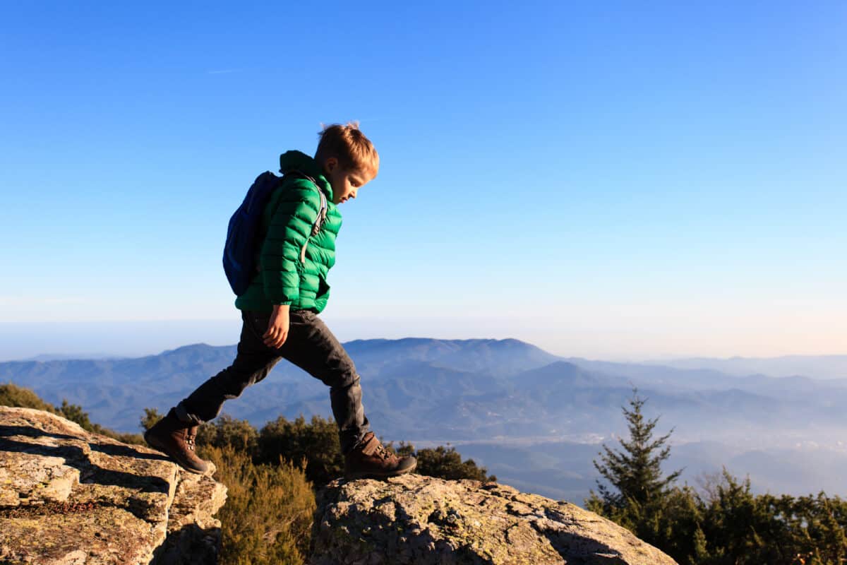 little boy with backpack hiking in scenic mountains