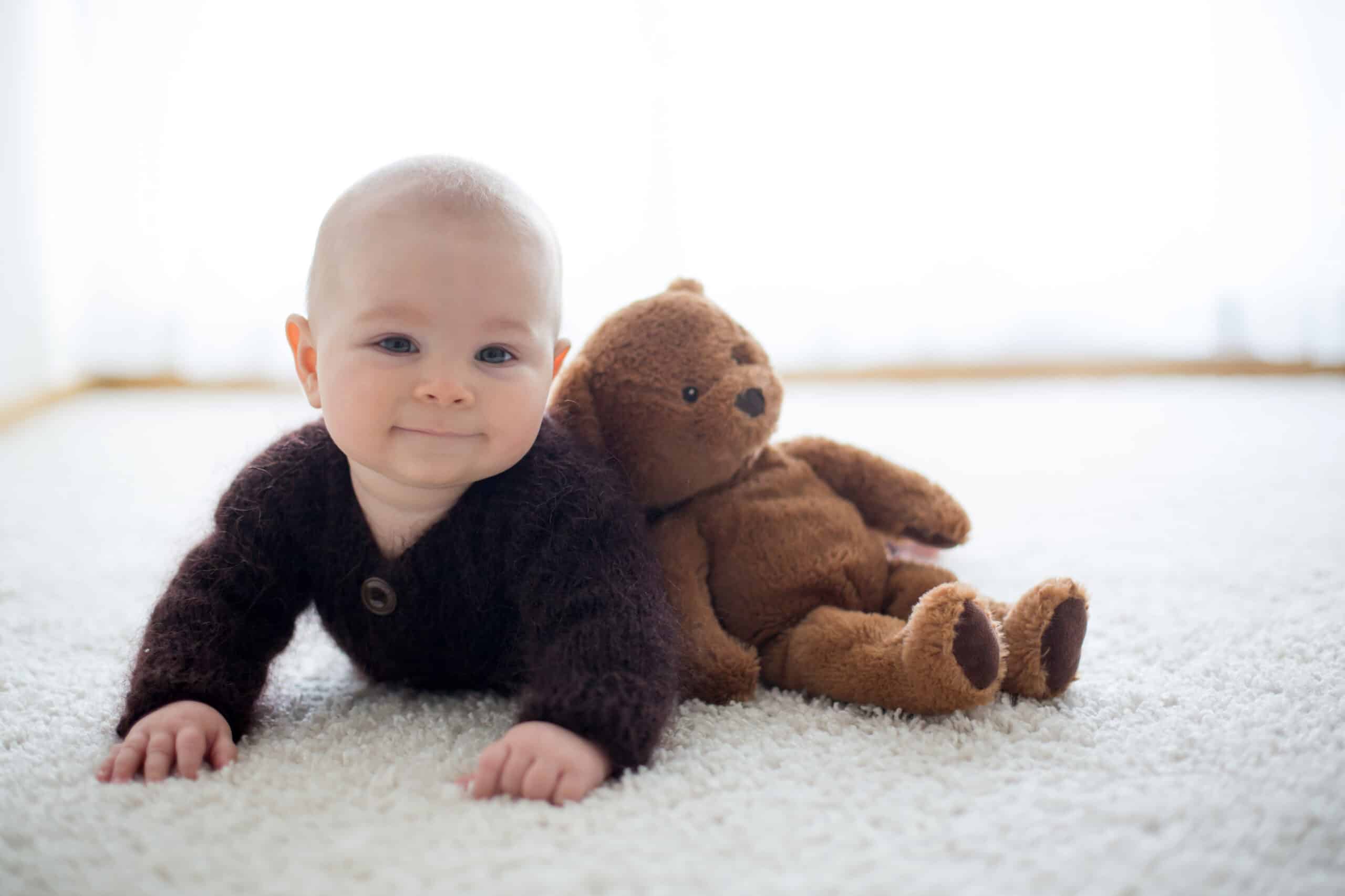 Little cute baby boy, dressed in handmade knitted brown teddy bear overall, playing at home in sunny bedroom