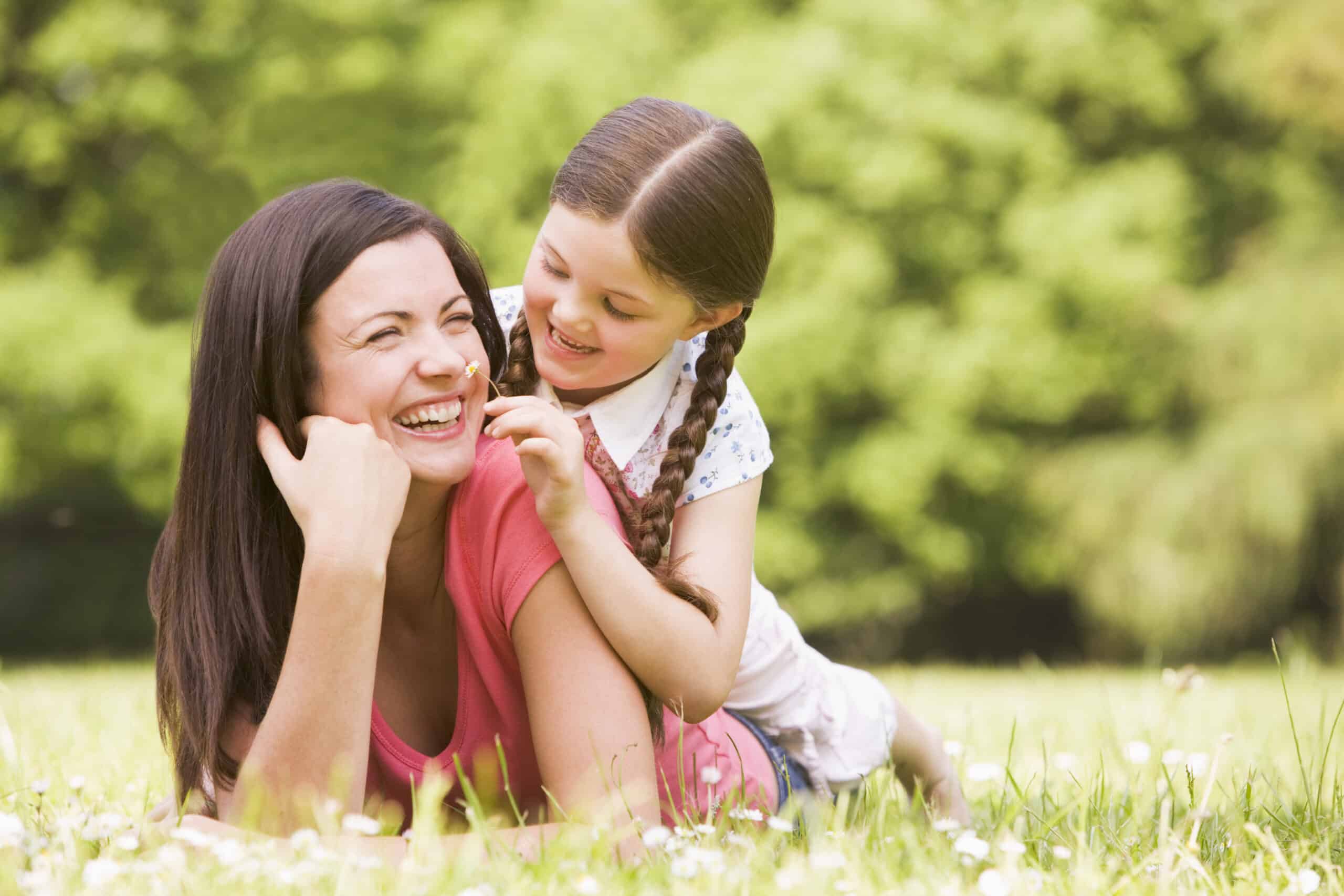 Mother and daughter lying outdoors with flower smiling