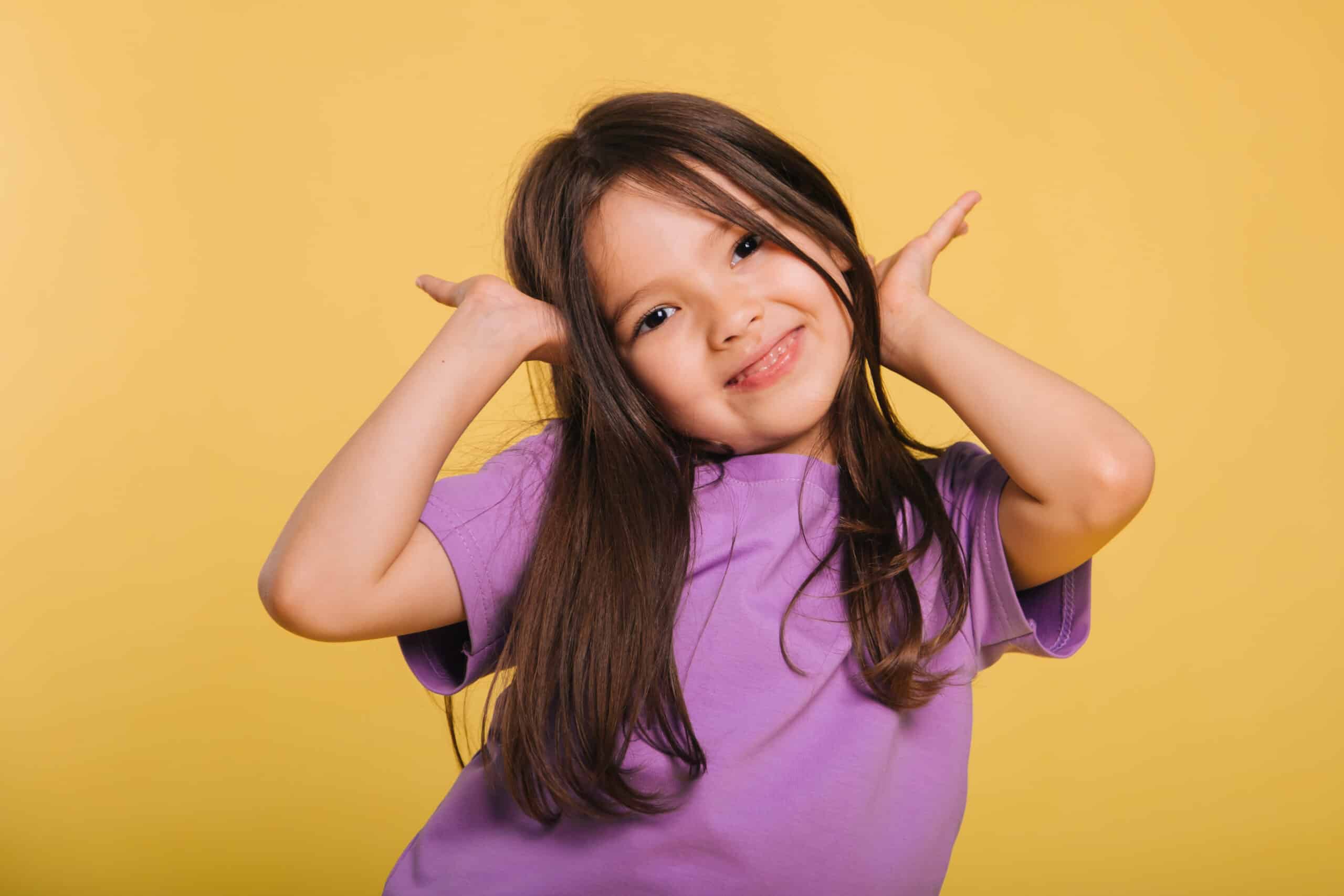 beautiful little girl in a purple t-shirt posing on a yellow background. Cute baby makes faces. Photo in studio