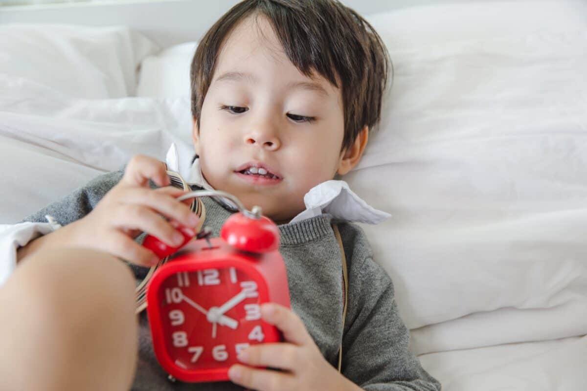 asian little boy holding an alarm clock in bed.