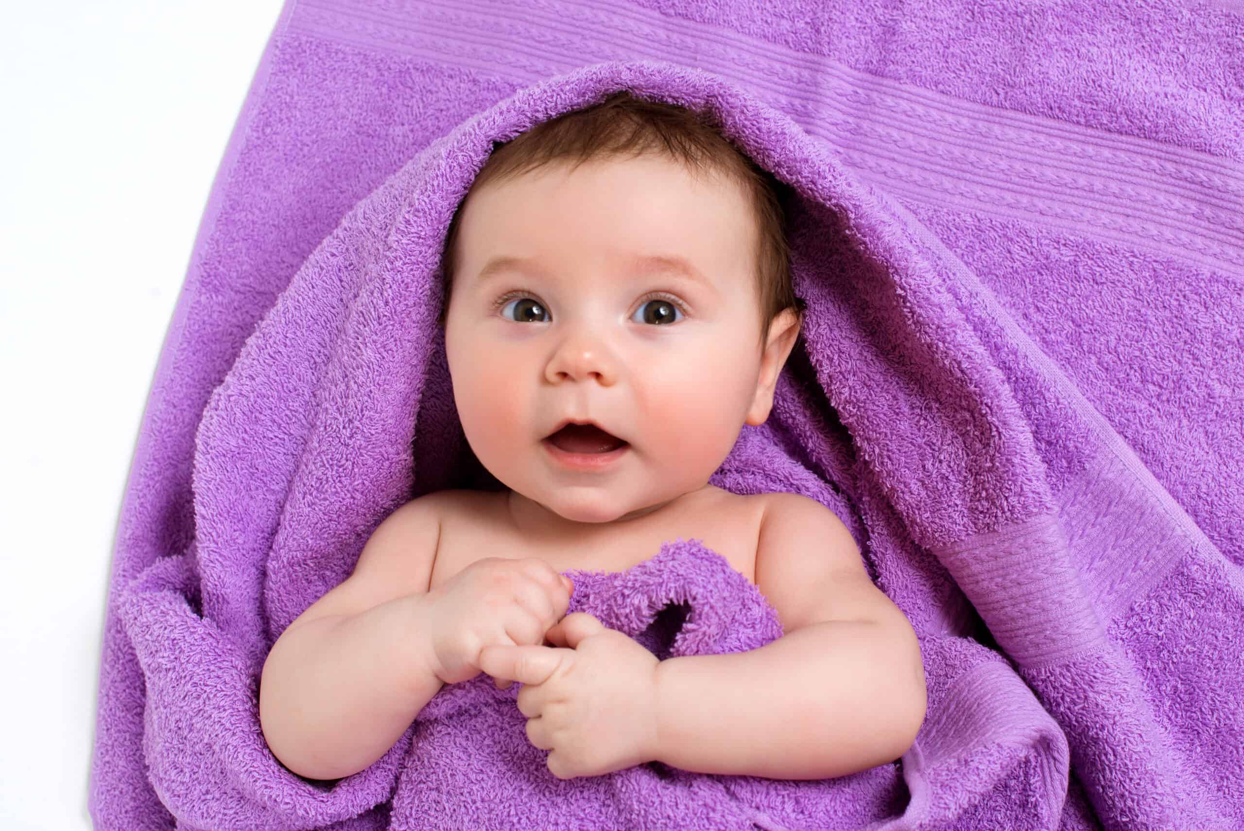 Newborn baby lying down and smiling in a purple towel