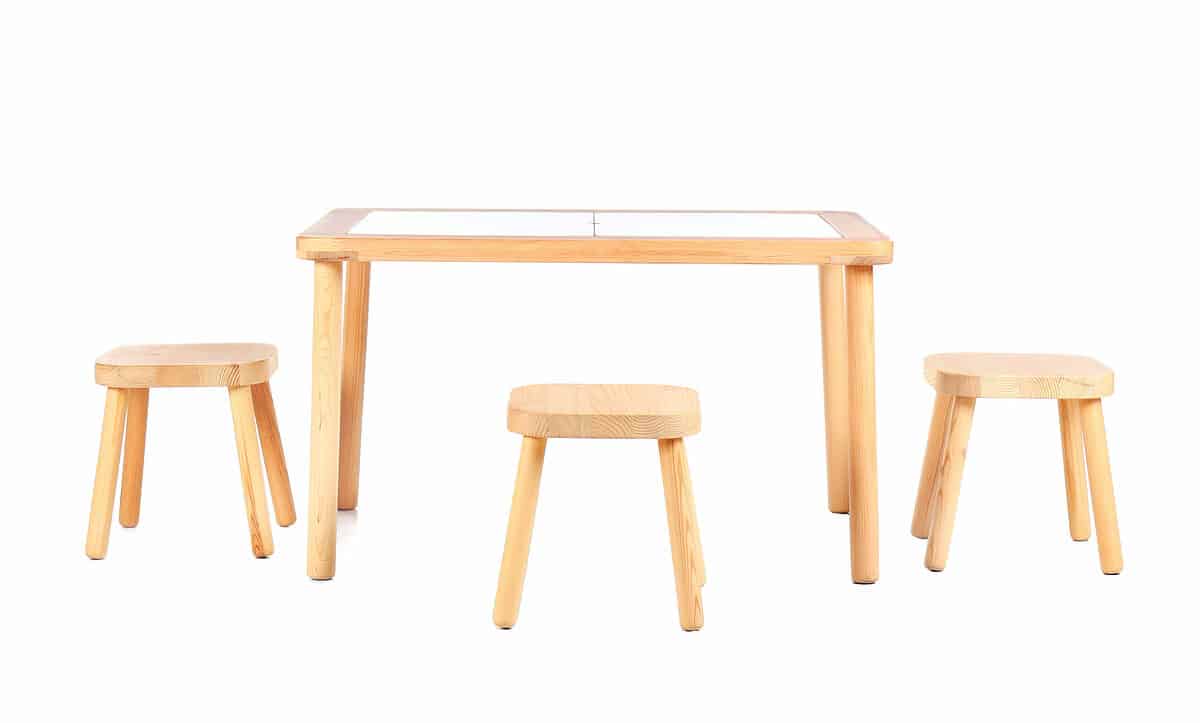 Three natural wood stools with four legs, slightly angled out are seen around a similar table made of natural wood with a white top. Against white isolate