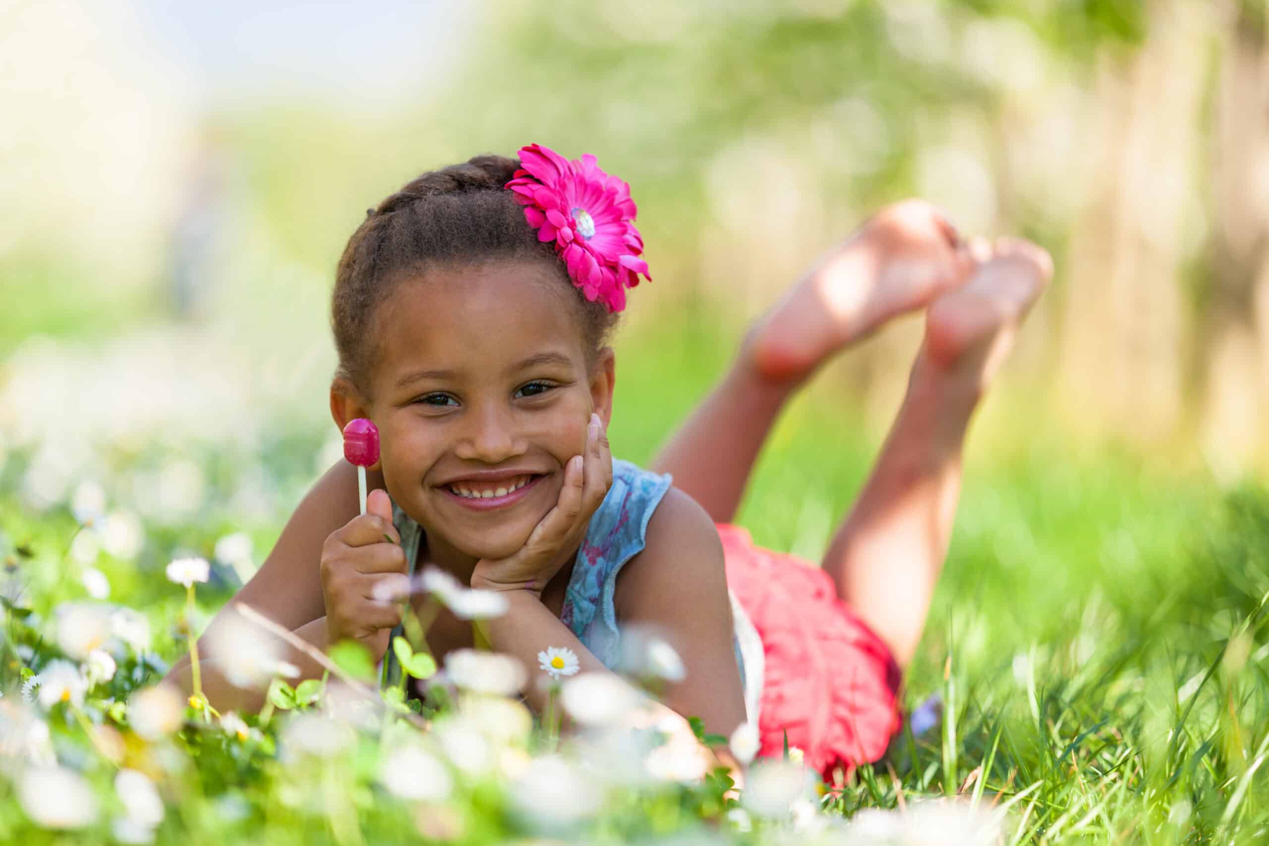 Outdoor portrait of a cute young black girl lying down on the grass and smiling - African people