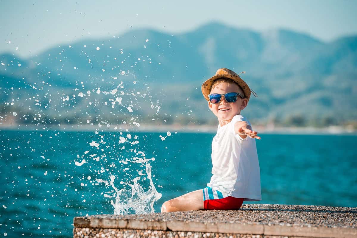 A happy little boy in blue sunglasses and hat has a big smile on his face. Beautiful landscape and bright beach. Blue summer sky and seawater background.