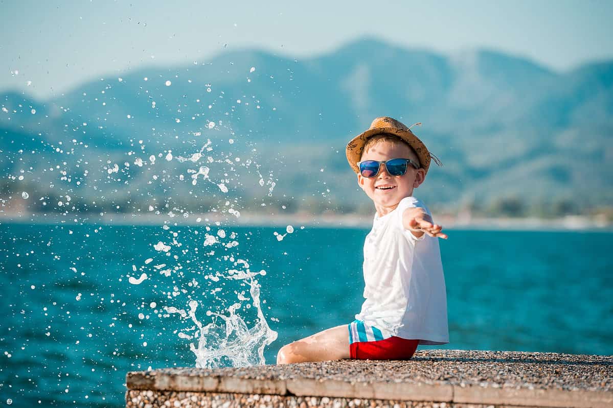 A happy little boy in blue sunglasses and hat has a big smile on his face. Beautiful landscape and bright beach. Blue summer sky and seawater background.