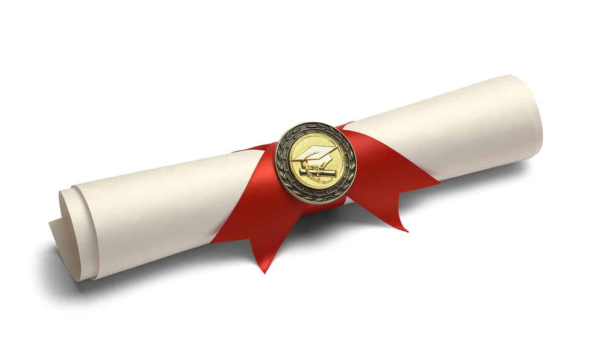 Photo of a rolled up piece of cream colored paper secured with a red ribbon in the center that’s probably an inch wide. The two ends of the ribbon are cut in a mountain shape (upside down V). Visible in the center of the ribbon is a gold medallion with a mortarboard (graduation cap with a tassel) and a tiny gold diploma. Against white isolate.