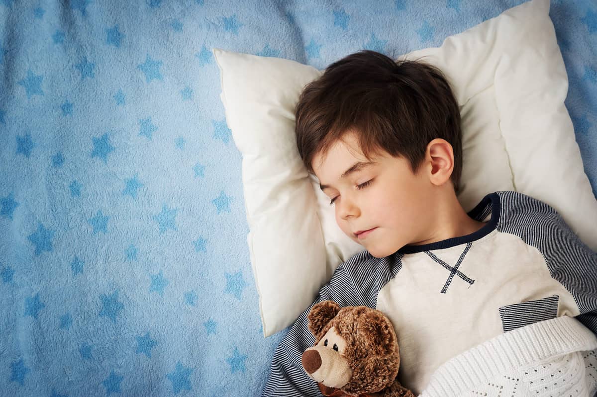 Six years old child sleeping in bed with an alarm clock