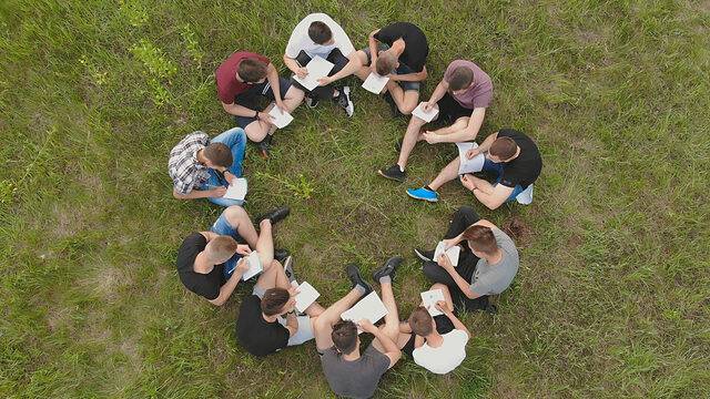 A group of high school students sits on the grass in a circle.
