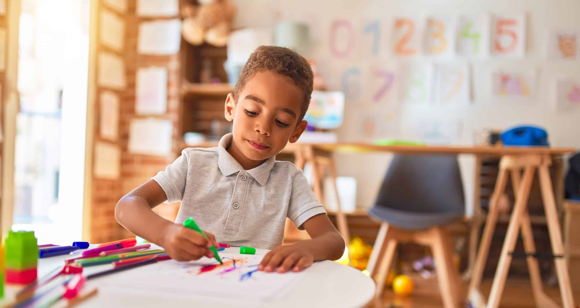 Young child uses marker and pen at a classroom table.