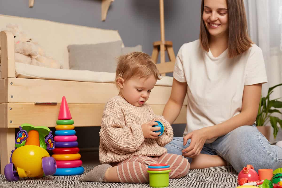 Young mother and little baby assembling plastic toys, method early development, confident family constructing toy tower use self educational game at home.