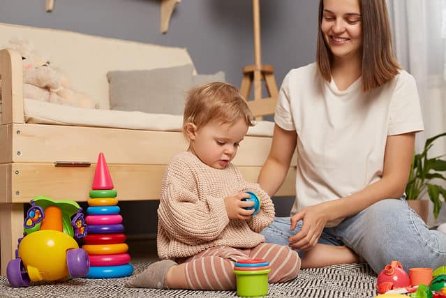 Young mother and little baby assembling plastic toys, method early development, confident family constructing toy tower use self educational game at home.