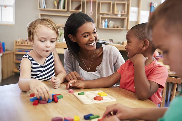 Teacher smiling and sitting with students in Montessori classroom.