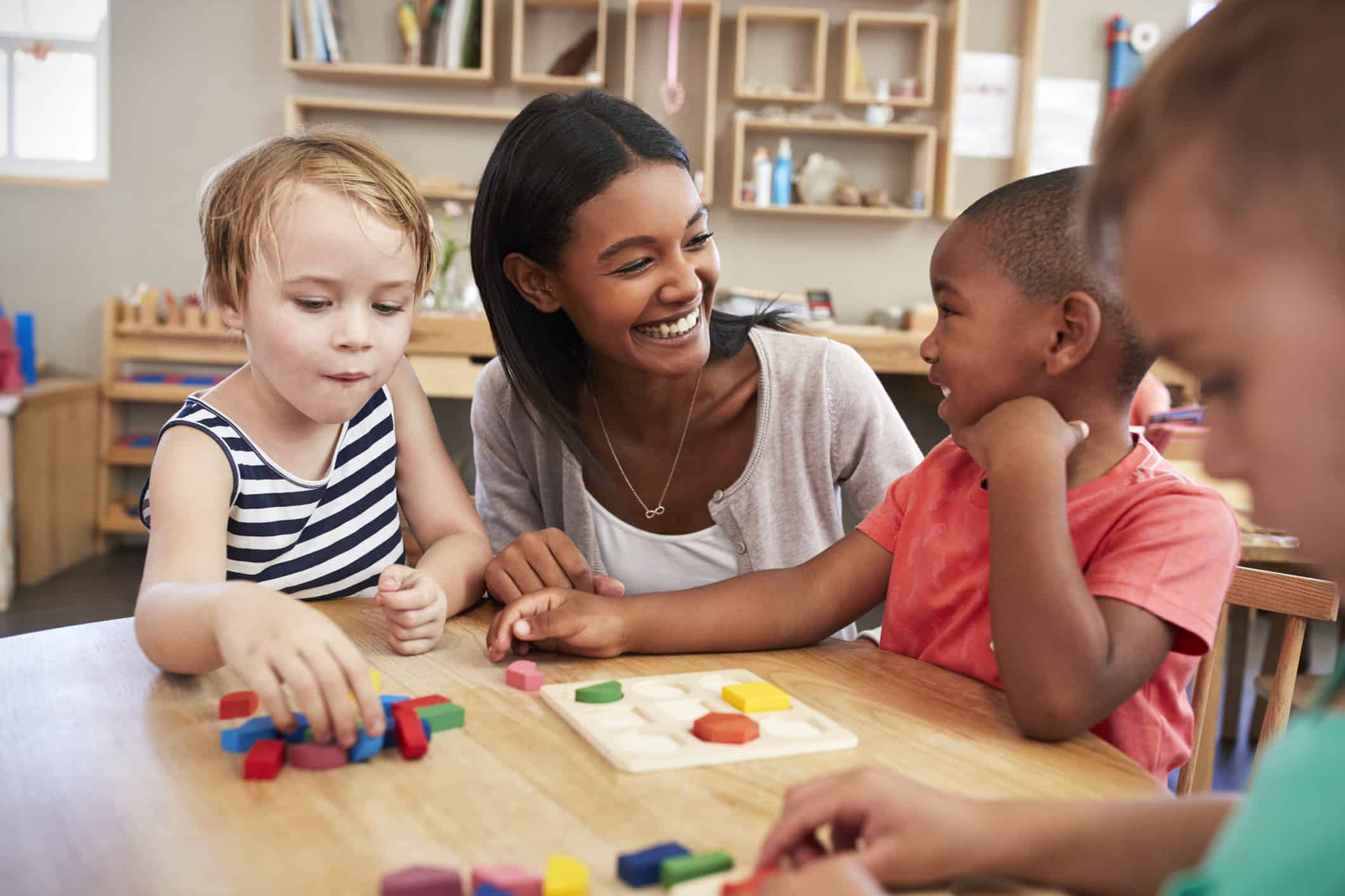 Teacher smiling and sitting with students in Montessori classroom.