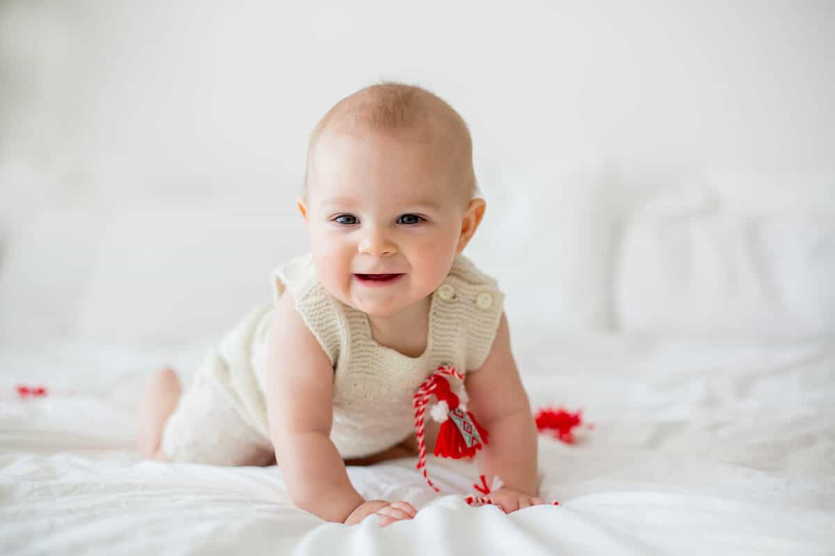 Cute baby toddler boy, playing with white and red bracelets. Martenitsa, white and red strains of yarn, Bulgarian folklore tradition, welcoming spring in March, adornment symbol, wish for good heath