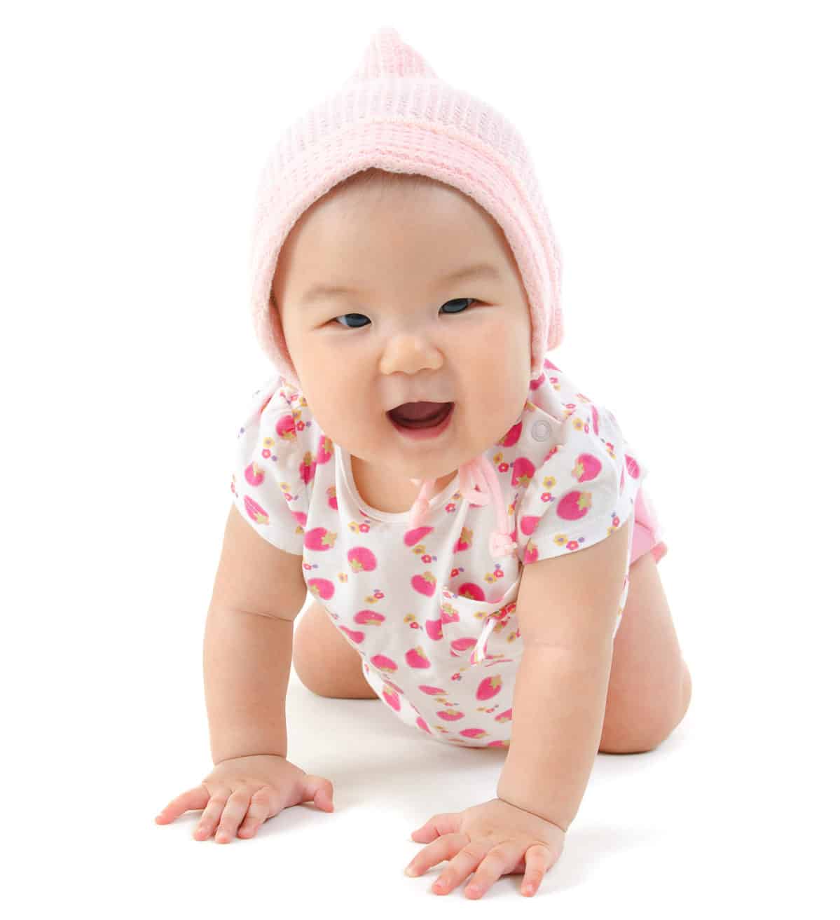 Six months old baby girl crawling over white background The boy is Asian appearing. She is wearing a light pink knitted cap ad a white short-sleeved onesie / romper with apink strawberry pattern.. Her mouth is open. She seems happy.