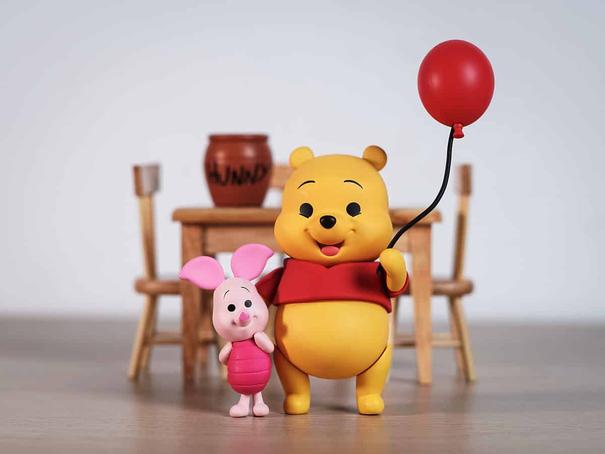 Winnie the Pooh holding a balloon in one hand and Piglets hand in the other hand.