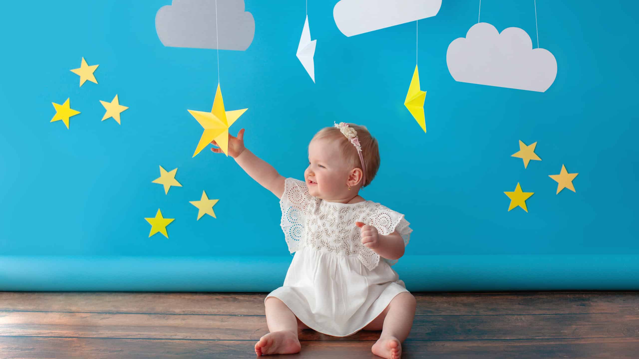 One year old baby celebrates birthday. Photo zone. Cute dress in white color. She touches a paper yellow star.