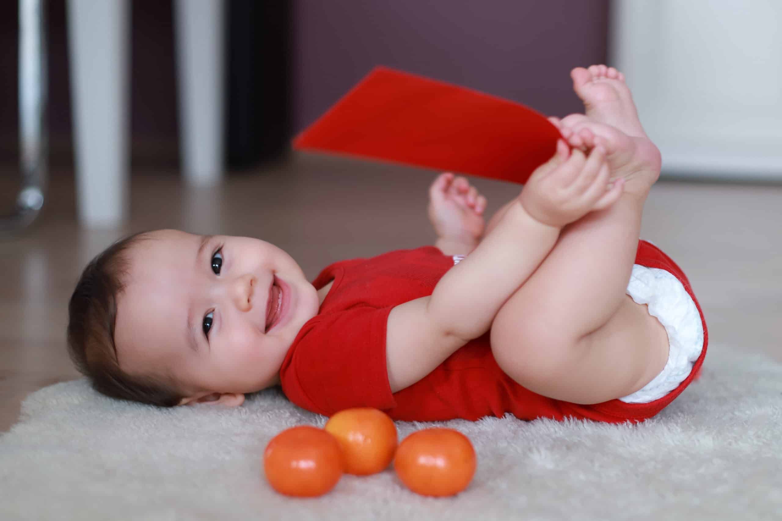 Cute baby boy holding a red envelope lying next to fresh mandarin orange with a smiling face concept for the Chinese lunar new year celebration. Happy mixed-race Asian-German infant.