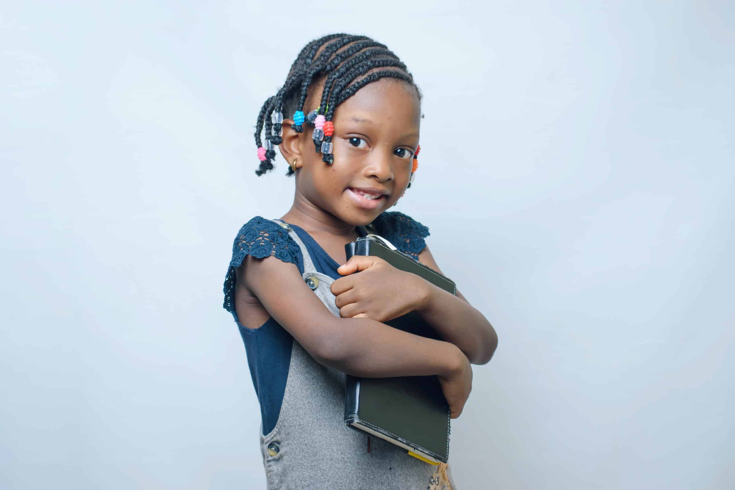 African girl child happily hugging and embracing educational books indoors as she believes education increases intelligence and knowledge which can be gotten from studying, reading, and learning