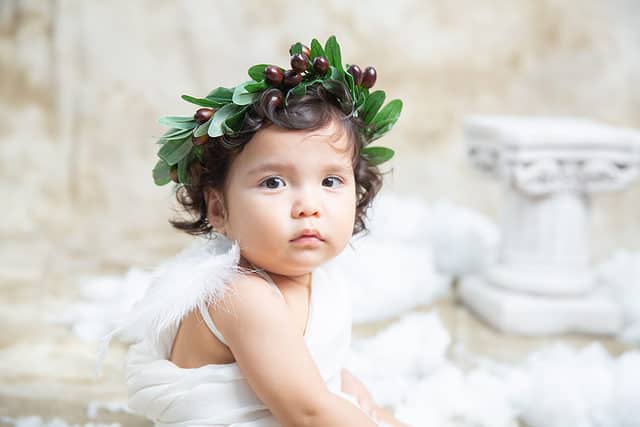 Cute beautiful baby. A mix of Chinese and Caucasian. Sitting on the chair and posing for the camera. Smiling, happy, and playing. Dressed in toga like a Greek god
