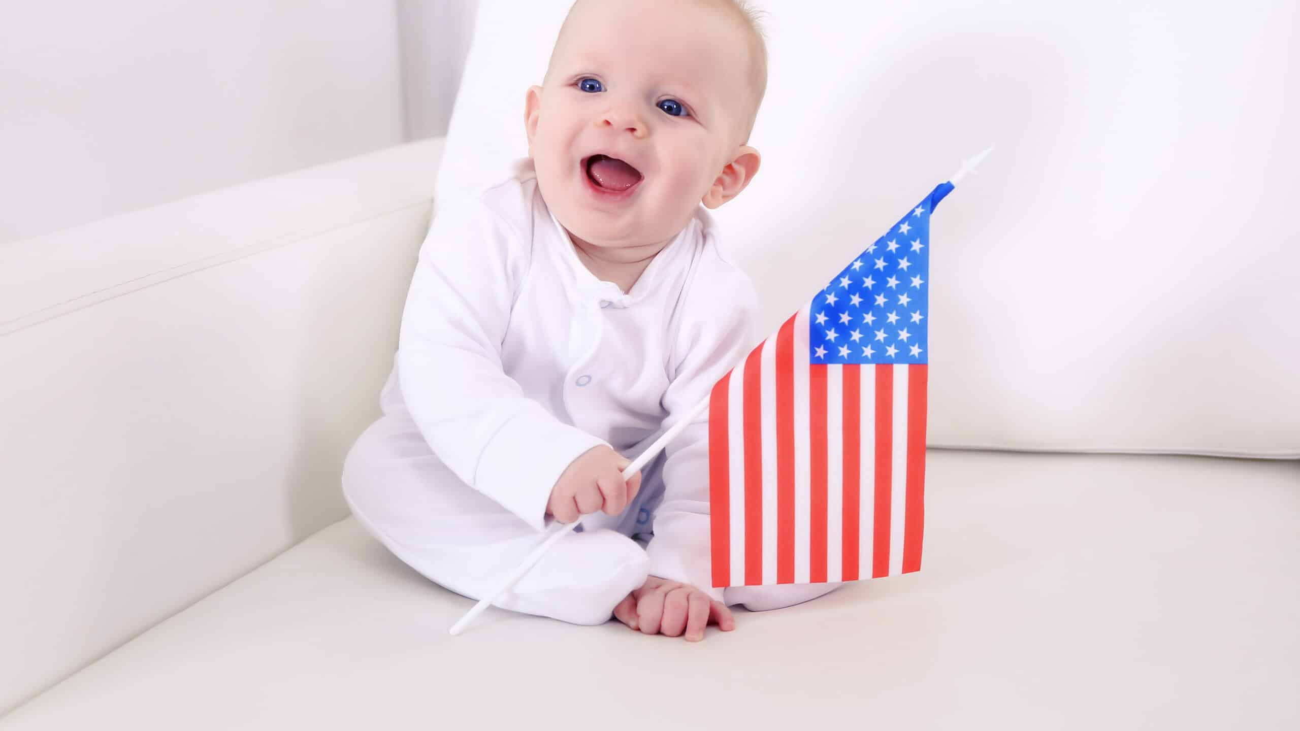 Cute baby boy on white couch with American flag, closeup