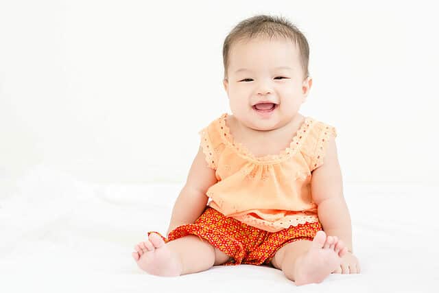 Portrait of a little adorable infant baby girl sitting on the bed and smiling to the camera with copy space