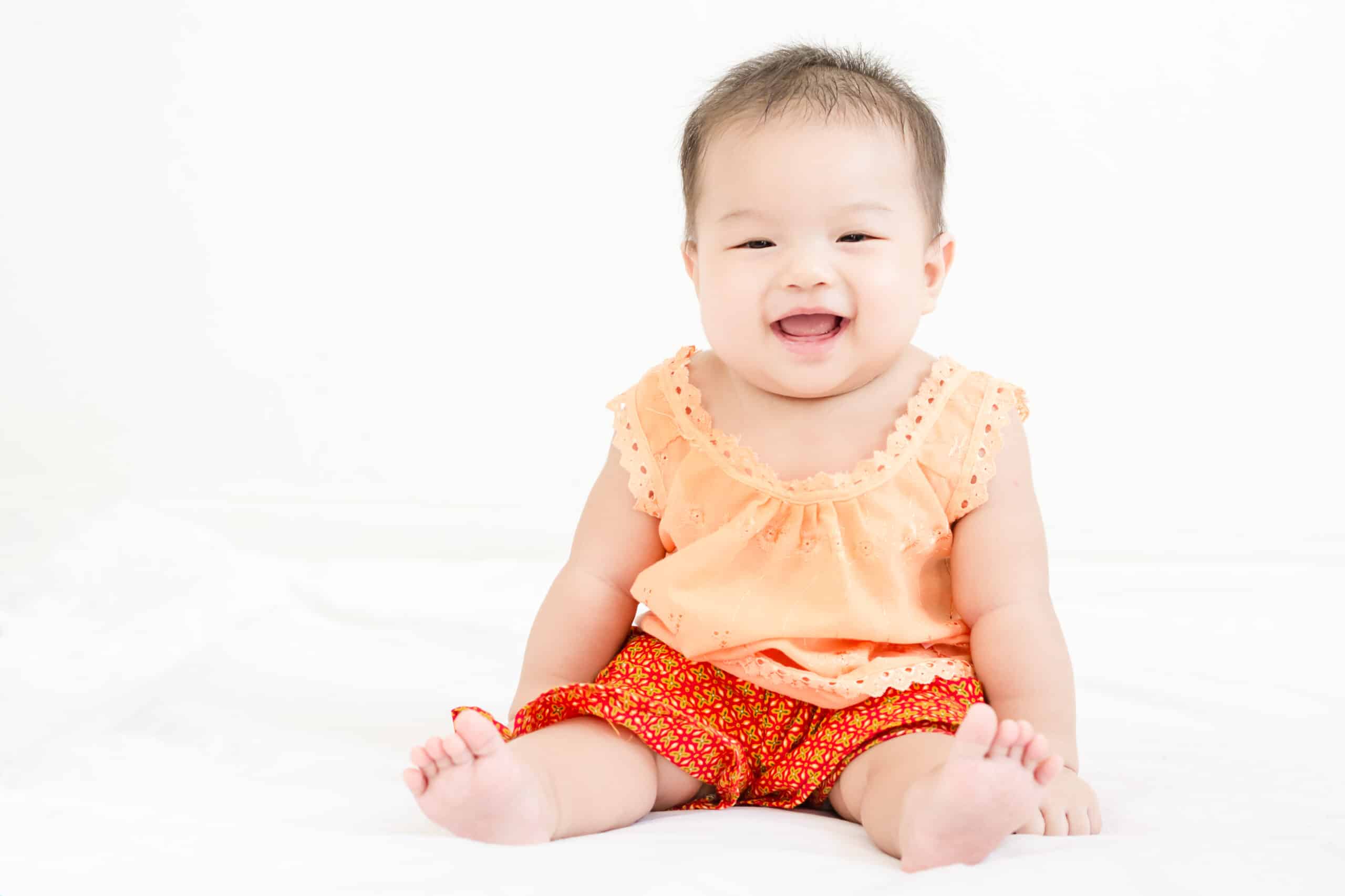 Portrait of a little adorable infant baby girl sitting on the bed and smiling to the camera with copy space