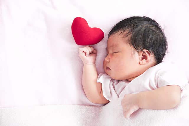 Cute Asian newborn baby girl sleeping with a red heart in bed