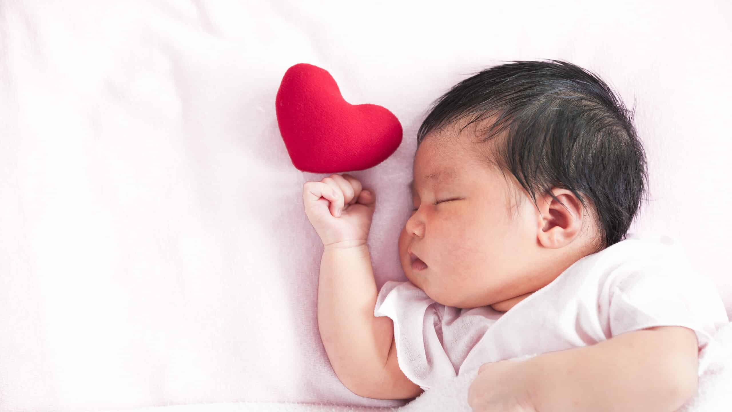 Cute Asian newborn baby girl sleeping with a red heart in bed