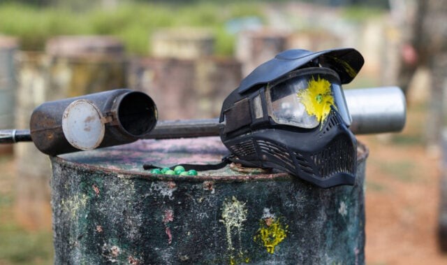 Closeup of black paintball mask with splash after direct hit from marker gun after match outdoors