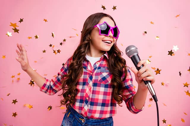 Little girl singing in a microphone with star glasses on and glitter around her