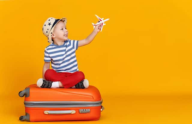 Little boy sitting on luggage and flying an airplane