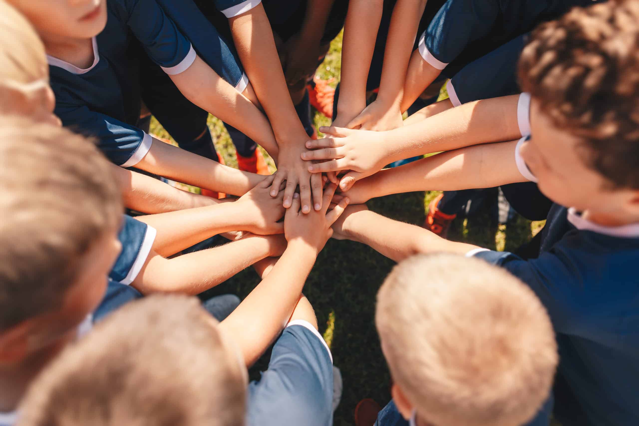 Happy kids sports team stacking hands at the field. Children team sports. Boys at sports camp stacking hands before a match. School age children in a team